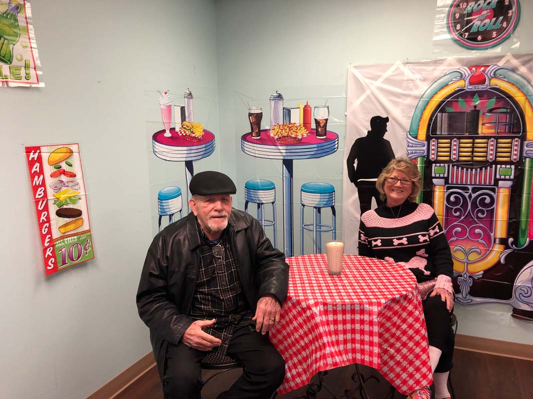 Two people smile in a room decorated as a 1950's diner.